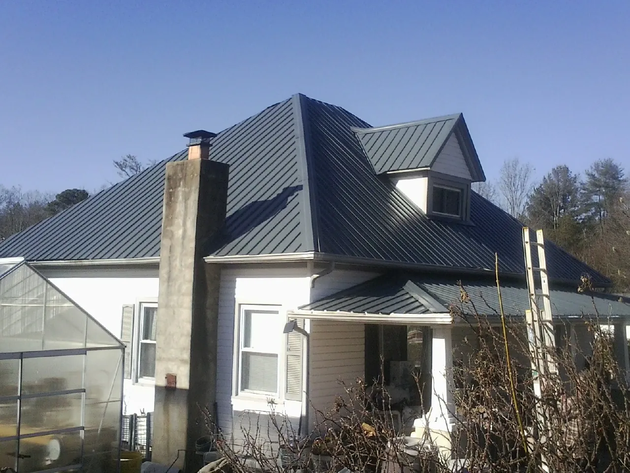 Dark blue standing seam metal roof on a white farmhouse with dormer — Slate & Tile Roof Repair by Roofing Brothers in Ferdinand