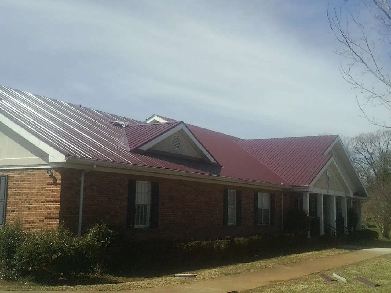 Red metal roof with gabled entries on a long brick building, from a Hail Damage Roof Repair job in Ferdinand
