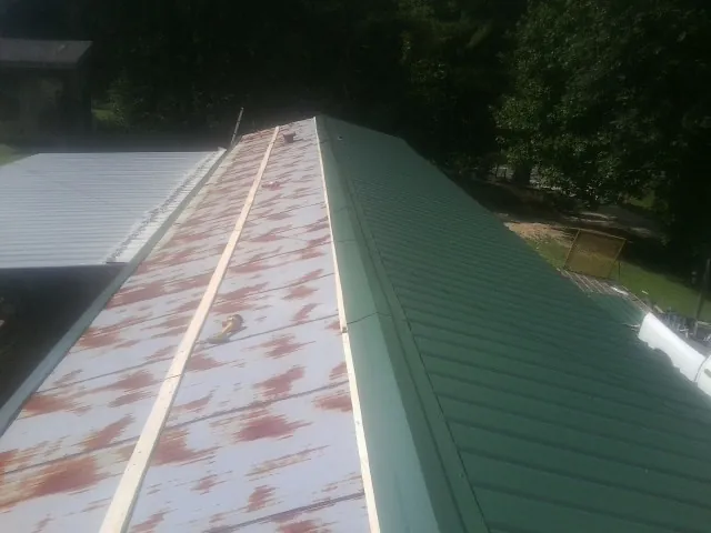Old rusted panels beside newly installed green metal roofing — Wind Damage Roof Repair by Roofing Brothers in Ferdinand