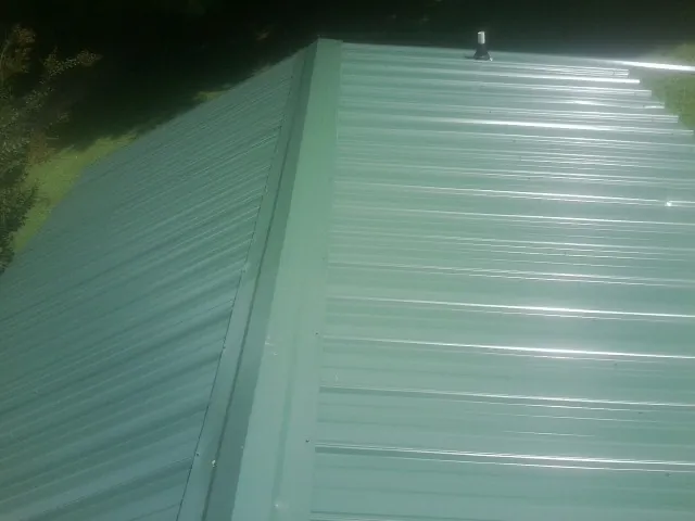 New green metal panels meeting at the ridge of a roof — Flat Roof Repair work by our crew in Ferdinand