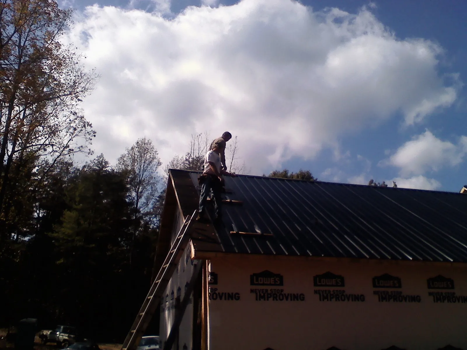 Roofer fastening dark metal panels high against a cloudy sky, from a Roof Inspection job in Ferdinand