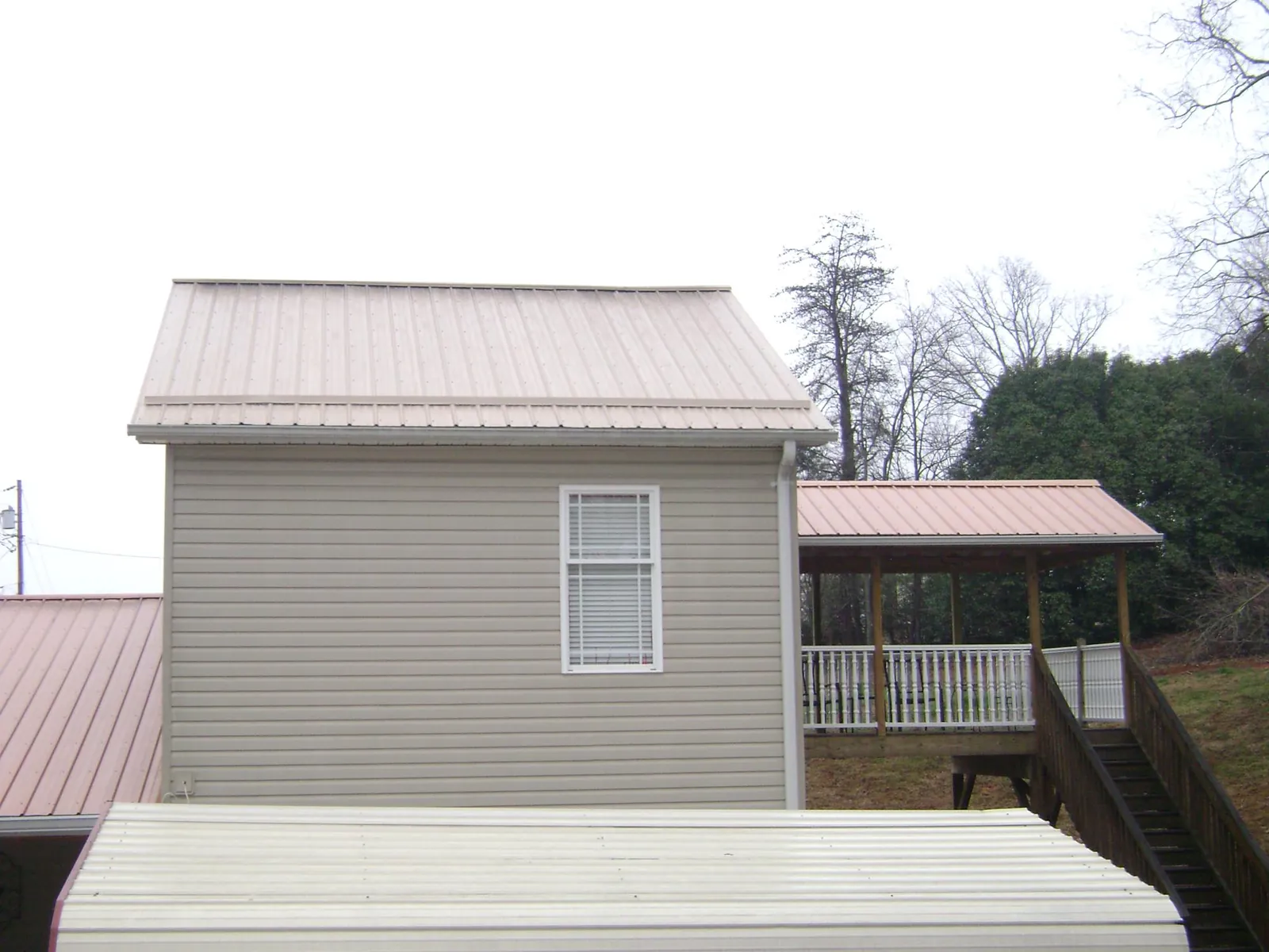 Tan metal roofs on a two story addition and attached porch, from a Roof Replacement job in Ferdinand